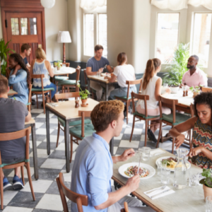 People dining in a bright, modern restaurant with wooden tables and chairs, enjoying meals and conversation in a casual café atmosphere during daytime.
